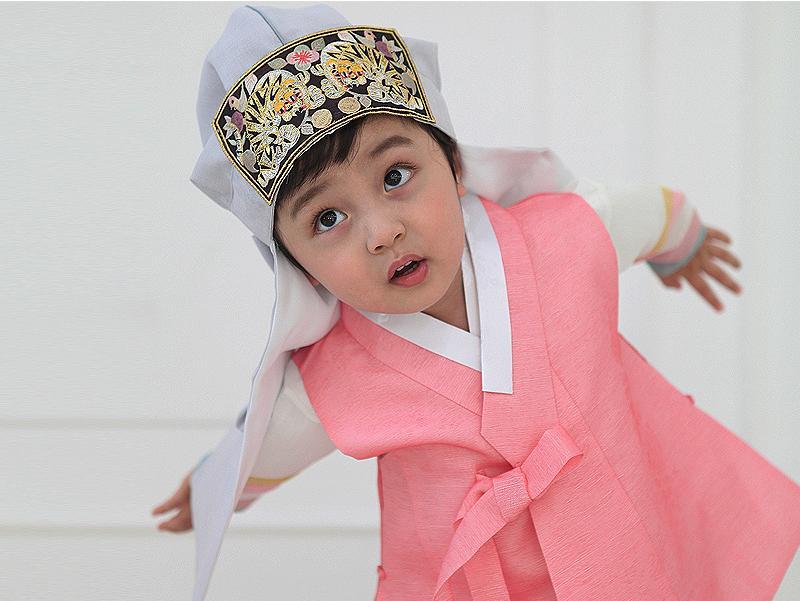 Young boy wearing a pink and gray korean hanbok and looking up