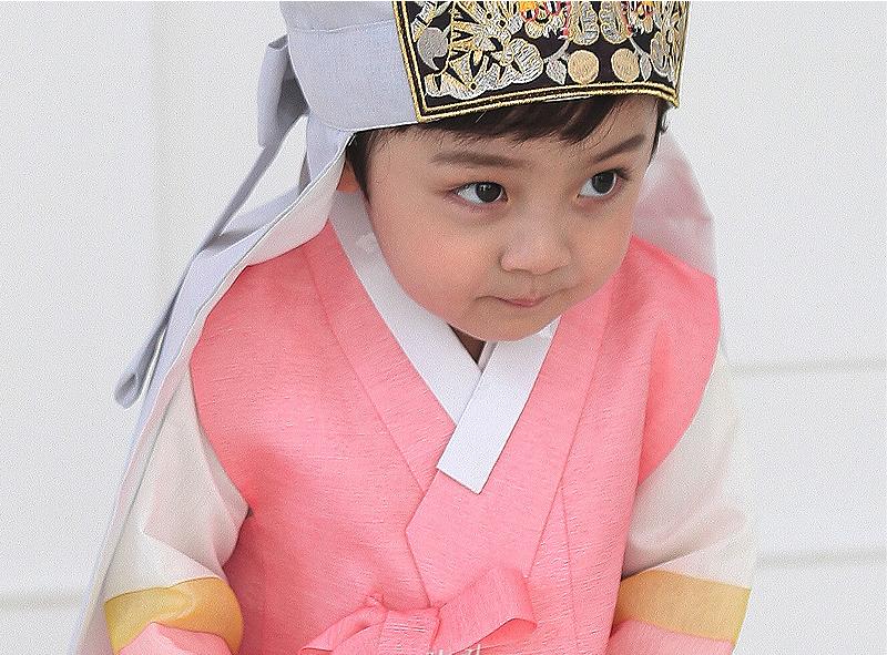 Young boy wearing a pink and gray korean hanbok with hat