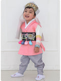 Young boy wearing a pink and gray korean hanbok and smiling