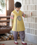 Young boy wearing a yellow and purple korean hanbok looking down