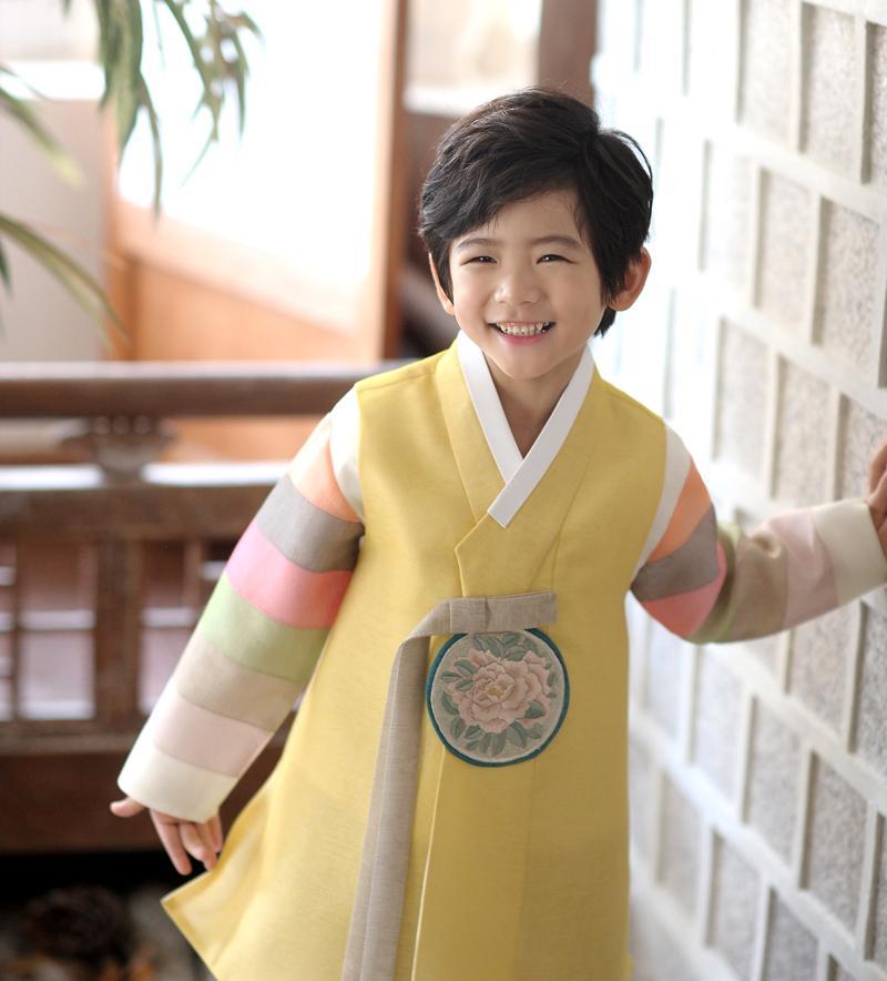 Young boy wearing a yellow and purple korean hanbok while smiling