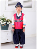 Young boy wearing a bright pink hanbok and navy hat standing next to flowers