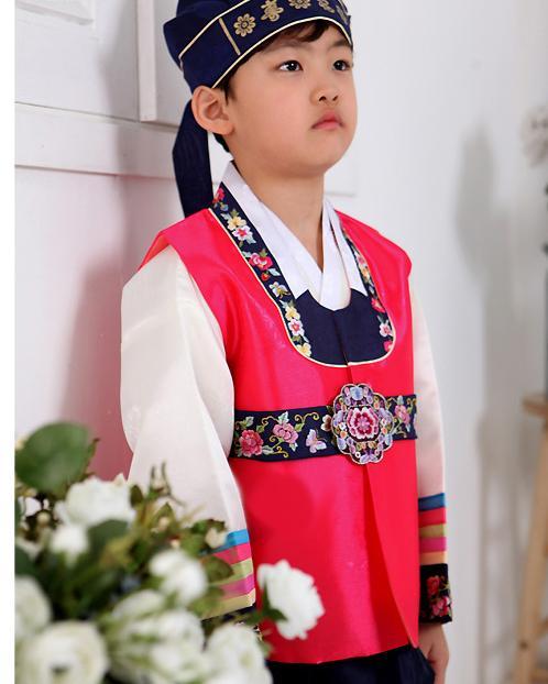 Young boy wearing a bright pink hanbok and navy hat and standing