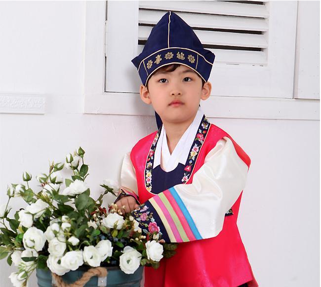 Young boy wearing a bright pink hanbok and navy hat