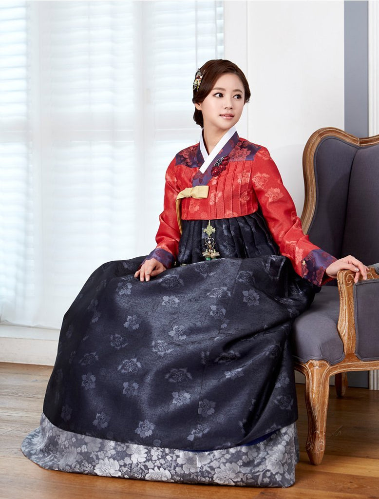 Woman wearing custom mother of the bride hanbok with red top and navy skirt while sitting down