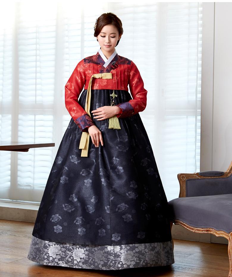 Woman wearing custom mother of the bride hanbok with red top and navy skirt looking down