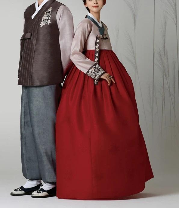 Woman wearing custom mother of the bride hanbok with rose top and red skirt standing next to a man