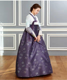 Woman wearing custom mother of the bride hanbok with white top and purple skirt and looking down