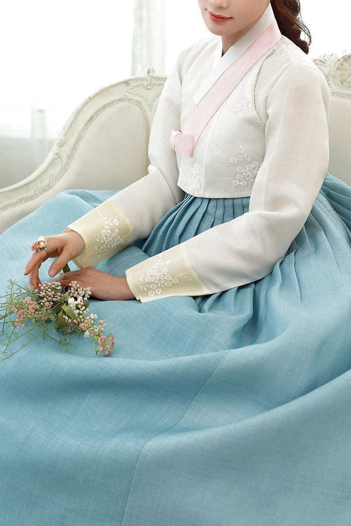 Woman sitting and wearing a custom womens bridal hanbok with white top and blue skirt