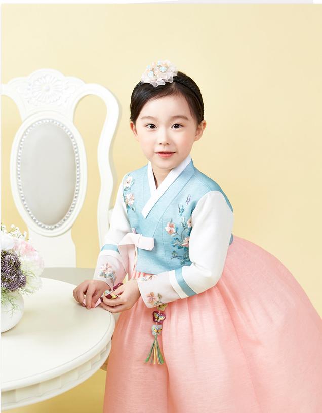 Young girl standing near table and wearing a girls korean hanbok with blue floral top and pink skirt