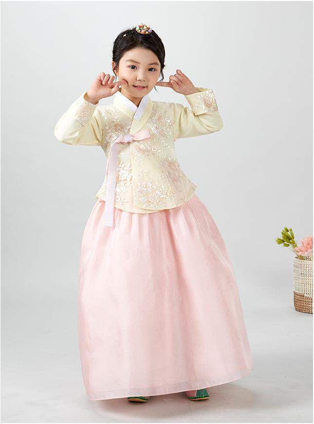 Young girl pointing at cheeks and wearing a girls korean hanbok with pastel yellow top and pink skirt